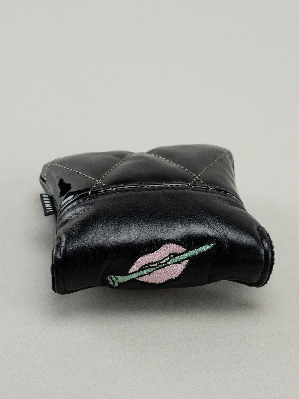 Black quilted leather golf headcover with top showing embroidered lips clutching a golf tee.
